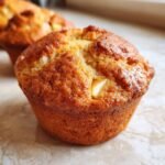 Close-up of a golden brown Apple Cinnamon Muffin with visible chunks of apple.