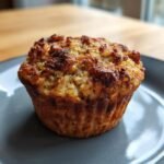 A close-up of a perfectly baked Banana Zucchini Muffin on a gray plate.