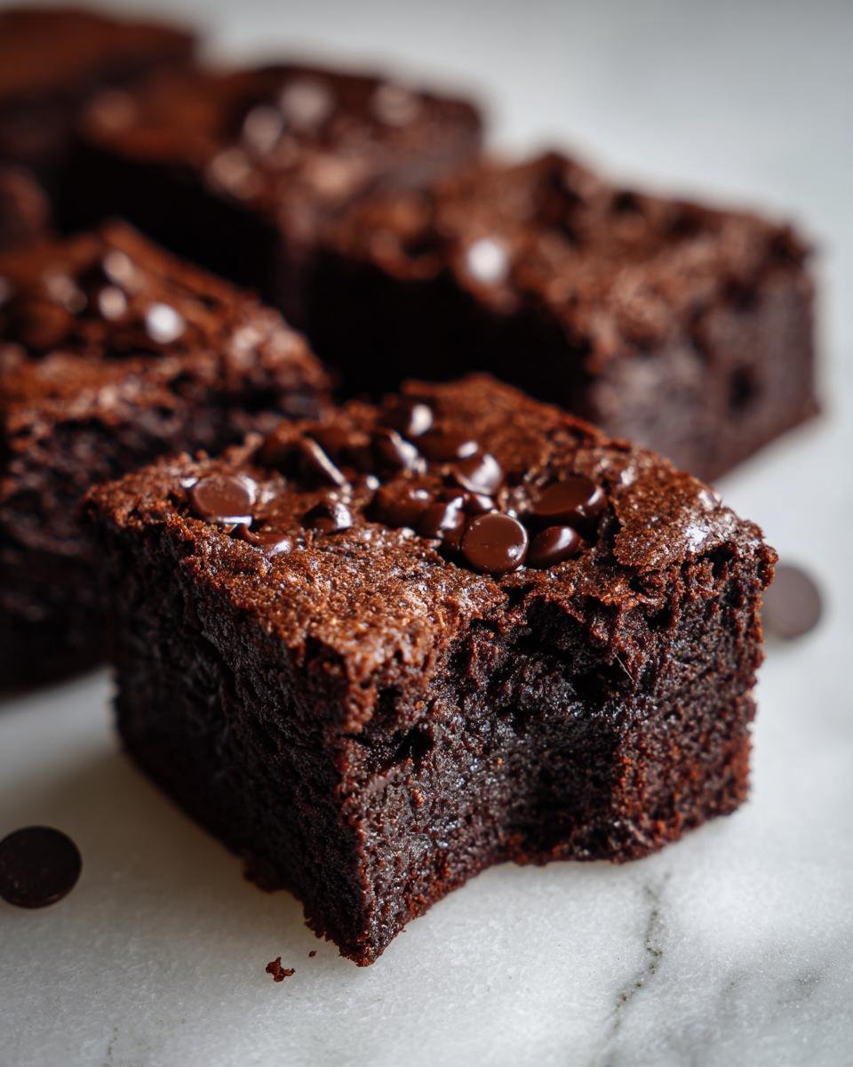 Close-up of a rich, fudgy Copycat Starbucks Double Chocolate Brownie topped with chocolate chips, with a bite taken out.
