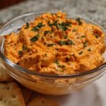 A bowl of creamy red pepper treats dip garnished with parsley, served with crackers.