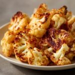A close-up shot of a plate filled with perfectly Crispy Roasted Cauliflower with Paprika, showing golden-brown florets with charred edges.