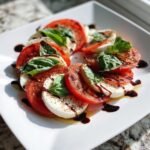 A beautiful arrangement of Delicious Caprese Salad with sliced tomatoes, fresh mozzarella, basil leaves, and drizzled with balsamic glaze.