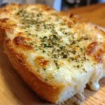 Close-up of a slice of delicious garlic bread pizza toast snack, topped with melted cheese and herbs.