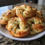 A plate piled high with golden-brown, freshly baked Delicious Garlic Knots Homemade Bread Treat, sprinkled with parsley.