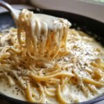 A fork lifts a swirl of fettuccine pasta coated in creamy, delicious homemade Alfredo sauce, seasoned with black pepper.