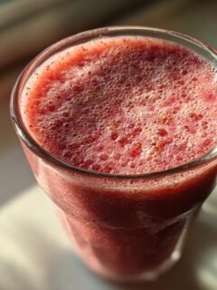 Close-up of a refreshing red berry smoothie in a glass, topped with foam and small seeds.