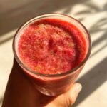 A hand holds a glass filled with a vibrant red smoothie, part of 5 Delicious Smoothies for the Week.