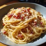 A close-up of a bowl of Delicious Spaghetti Carbonara, a creamy Italian classic, topped with crispy pancetta and grated cheese.
