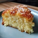 A slice of Dreamy Pineapple Coconut Cake topped with toasted coconut flakes, on a light blue plate.