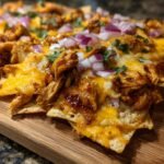Close-up of Flavorful BBQ Chicken Nachos topped with melted cheese, shredded chicken, and red onions.