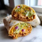Close-up of a Flavorful BBQ Chicken Wrap cut in half, revealing shredded chicken, cheese, lettuce, and red onion.