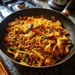 A close-up overhead view of flavorful chicken stir fry noodles in a black skillet, featuring tender chicken pieces and vibrant vegetables.