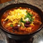 A close-up of a hearty bowl of Flavorful Chicken Taco Soup, topped with shredded cheese, onions, and cilantro.