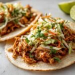 Close-up of two Flavorful Chicken Tacos With Lime Cilantro Slaw, showcasing shredded chicken and fresh slaw on tortillas.