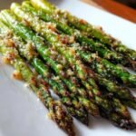 Close-up of Flavorful Roasted Garlic Parmesan Asparagus on a white plate, showing crisp edges and a cheesy topping.