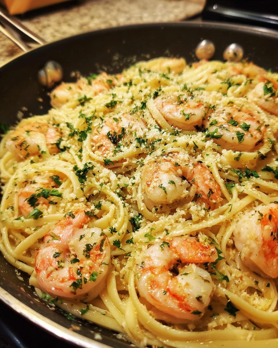 Close-up of Flavorful Shrimp Alfredo Linguine pasta dish in a pan, topped with shrimp, parsley, and cheese.