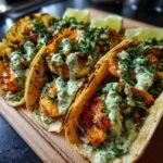 Close-up of three Flavorful Shrimp Tacos With Avocado Crema, garnished with fresh cilantro and lime wedges.