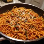 A close-up of a pan filled with Flavorful Tomato Basil Pasta, topped with fresh basil and grated Parmesan cheese.