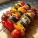 Close-up of grilled vegetable brochette skewers featuring zucchini, bell peppers, red onion, and cherry tomatoes seasoned with herbs.