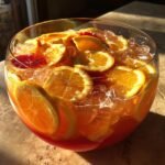 A close-up of a large glass bowl filled with Hawaiian Punch, ice, and slices of oranges and blood oranges.