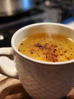 A steaming mug of golden Healing Cinnamon Turmeric Tea, sprinkled with spices.