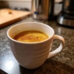 A close-up of a steaming mug of Healing Cinnamon Turmeric Tea, sprinkled with cinnamon.