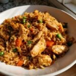A close-up of a bowl filled with flavorful Hibachi Style Chicken Fried Rice, featuring tender chicken pieces, peas, and carrots.