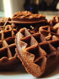 A close-up shot of a stack of delicious homemade chocolate waffles on a white plate.