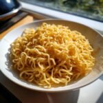 A close-up of a white bowl filled with golden, freshly made homemade egg noodles.