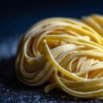 A close-up, artistic shot of a nest of fresh homemade egg noodles dusted with flour.