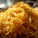 A close-up, sunlit pile of fresh, golden homemade egg noodles.