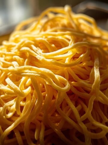 A close-up, sunlit pile of fresh, golden homemade egg noodles.