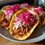 Close-up of three Irresistible BBQ Pulled Pork Tacos topped with vibrant pink pickled onions and slaw.