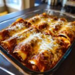 Close-up of Irresistible Cheesy Chicken Enchiladas baked in a glass dish, covered in red sauce and melted cheese.