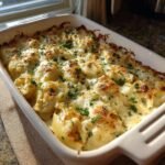 A close-up of baked Irresistible Chicken Alfredo Stuffed Shells in a white baking dish, topped with melted cheese and parsley.