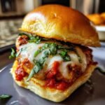 Close-up of an Irresistible Chicken Parmesan Slider, featuring a golden bun, melted mozzarella, marinara sauce, and fresh basil.