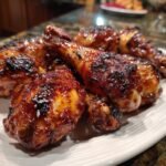 A close-up of a plate piled high with glistening Irresistible Honey BBQ Chicken Drumsticks, perfectly cooked.