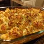 A close-up of a bubbling Keto Cauliflower Mac and Cheese casserole, topped with golden-brown cheese and herbs.