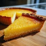 A close-up of a slice of moist lemon tart, showcasing its bright yellow filling and golden, slightly caramelized top.
