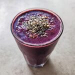 A glass of vibrant purple Nutritious Dinner Replacement Smoothie topped with chia seeds and other grains.