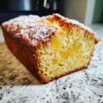 A close-up of a slice of Pineapple Quick Bread, showing chunks of pineapple within the moist crumb, topped with shredded coconut.