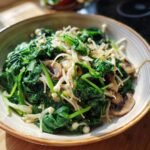 Close-up of a bowl filled with Sautéed Spinach and Enoki Mushrooms, with sliced mushrooms and onions.