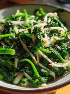 Close-up of a bowl filled with vibrant green sautéed spinach and delicate enoki mushrooms, seasoned with sesame seeds.