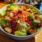 A vibrant bowl of Super Crunch Salad featuring crisp lettuce, shredded carrots, red onion, and golden croutons.