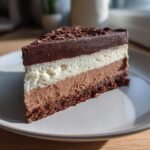 A decadent slice of Triple Chocolate Mousse Cake featuring three distinct layers of mousse and a chocolate base, topped with chocolate shavings.