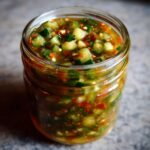 Close-up of a glass jar filled with Ultimate Easy Sweet Zucchini Relish, showing diced zucchini and red chili flakes.