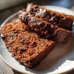Close-up of moist vegan chocolate zucchini bread slices on a plate, showing chocolate chips and green zucchini shreds.