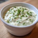 Close-up of creamy homemade Ranch Dressing topped with fresh, finely chopped green herbs in a small white bowl.