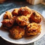 A pile of golden-brown crispy fried mushrooms, coated in breadcrumbs, on a white plate.