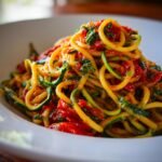 A close-up of a white bowl filled with Delicious Healthy Tomato Zucchini Pasta, showing spiralized zucchini noodles coated in a rich tomato sauce with herbs.